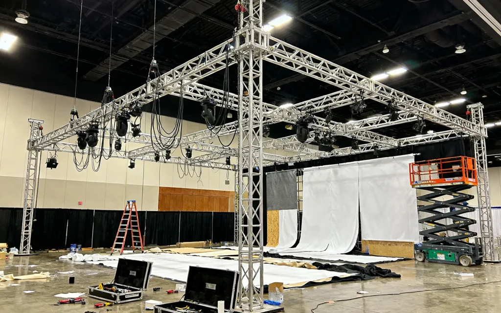 Truss-constructie tijdens de opbouw van een beursstand waarbij monteurs een wandbespanning aan het frame bevestigen.